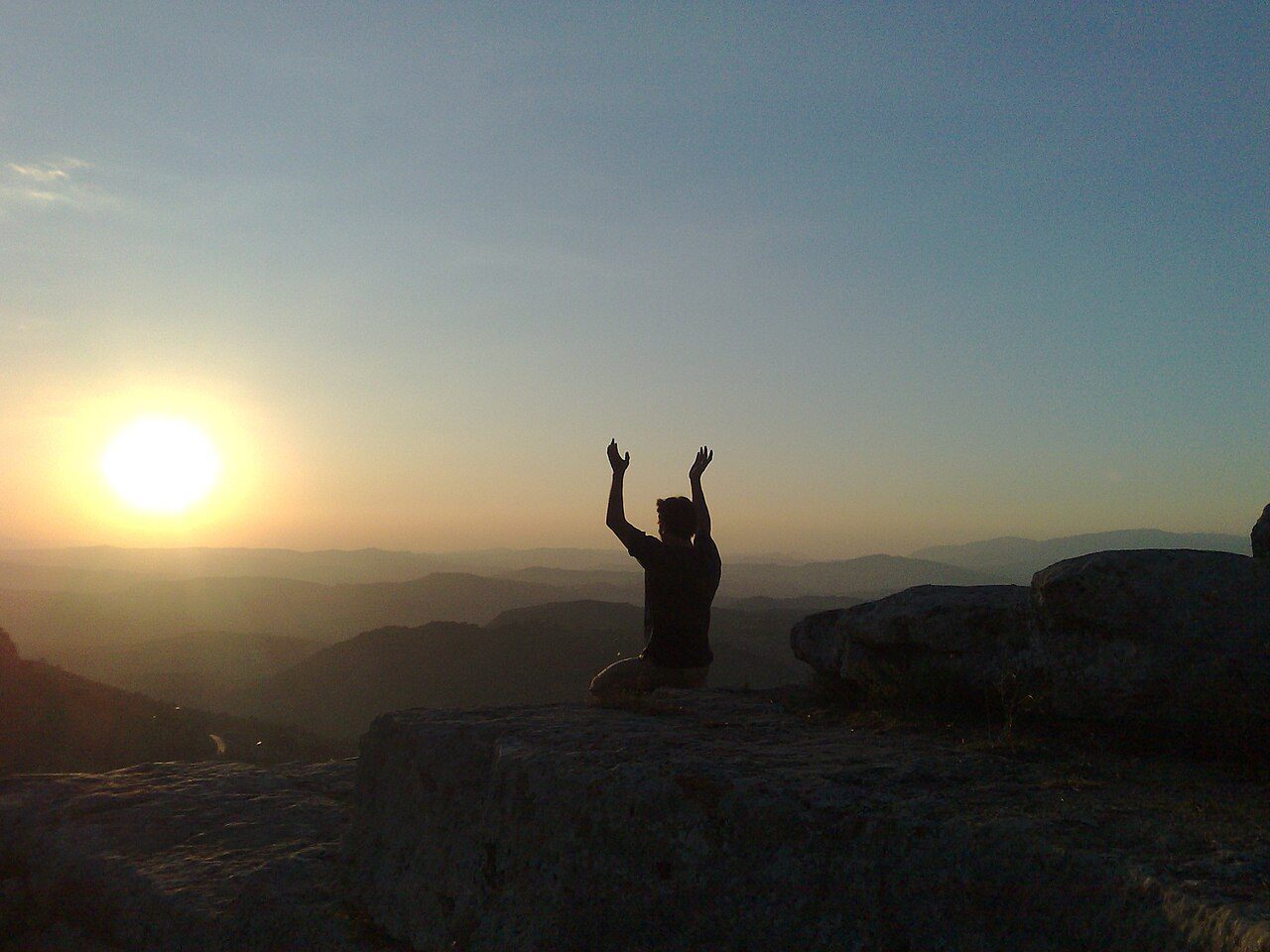 A meditator silhouetted against the sun above mountain ridges