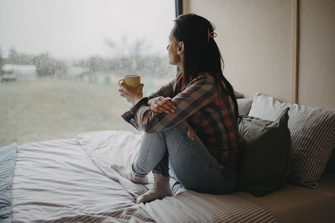 A woman holding a warm cup, watching rain at the window